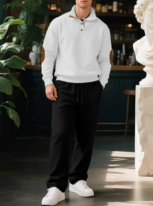 Dettaglio polo in maglia bianca con toppe marroni sui gomiti e pantaloni a righe