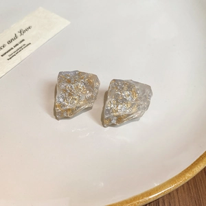 Detail of irregular resin stud earrings with gold foil accents on a decorative plate