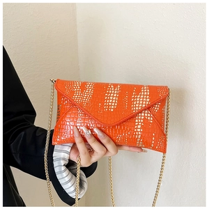 Close-up of orange crocodile pattern envelope bag with golden chain strap and white spots