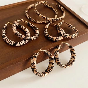 Close-up of four pairs of leopard print hoop earrings on a vintage dark wooden tray