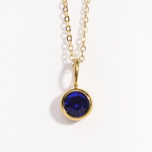 Close-up of a gold necklace with a round blue birthstone pendant on a white background