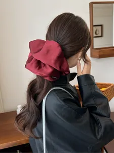 Detail of burgundy satin oversized scrunchie featuring a black fashion label on silk fabric