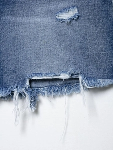 Macro shot of blue denim shorts showing distressed ripped holes and frayed hem detail