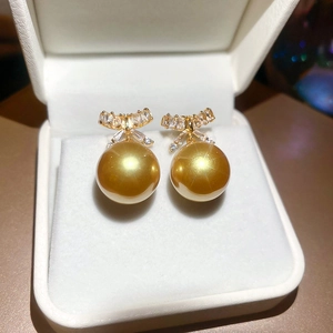 Detailed close-up of champagne pearl earrings with zircon bows in a luxury white gift box