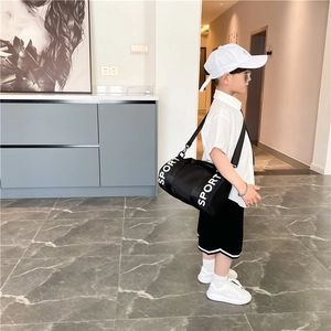 Close-up of child model wearing a black cylinder crossbody sport bag with white logo