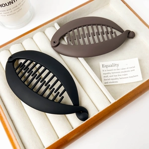 Matte black and brown banana hair clips with non-slip teeth on a wooden display tray