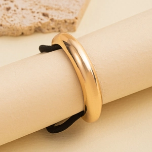 Close-up of minimalist gold metal hair ring with black elastic band on stone texture