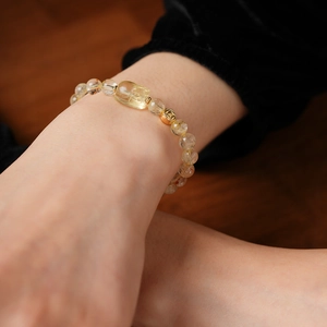 Macro shot of artificial rutilated quartz beaded bracelet with a gold coin charm on wrist