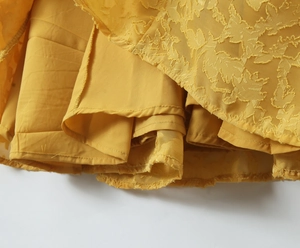 Detailaufnahme von gelbem Jacquard-Stoff und mehrlagigem Fischschwanz-Saumdesign
