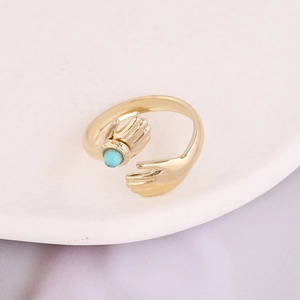 Detail of gold hug ring featuring hands holding a round turquoise stone on a tray