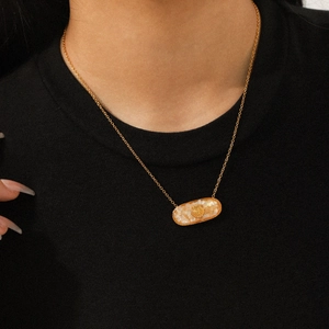 Detail view of oval gold necklace with shell inlay worn by a model on black background