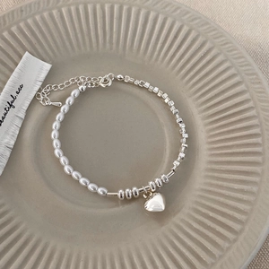 Detail of silver beaded bracelet with white pearls and heart pendant on ceramic plate
