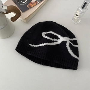 Close-up of black knit beanie with white jacquard bow pattern and ribbed cuff detail