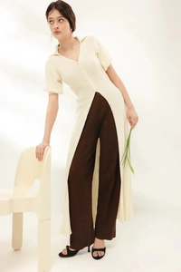 Detail of cream knit cardigan paired with dark brown pleated trousers in minimalist studio
