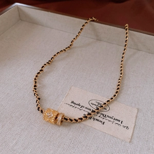 Detail of gold cylinder pendant with zircon clover on black leather chain necklace