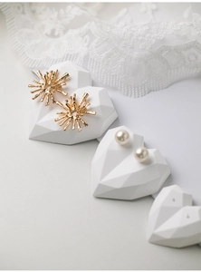 Detail of gold sunburst earrings and pearl studs on heart-shaped jewelry display stand