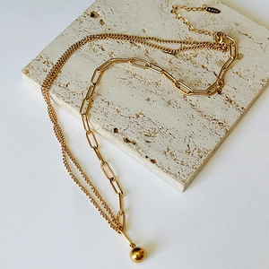 Detail of gold layered chain necklace with metal ball pendant on beige travertine stone
