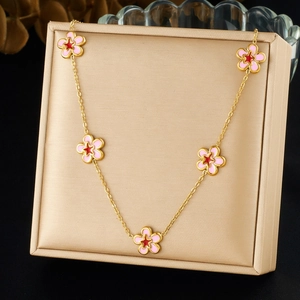 Detailed view of gold chain necklace with five pink enamel flower pendants in a display box