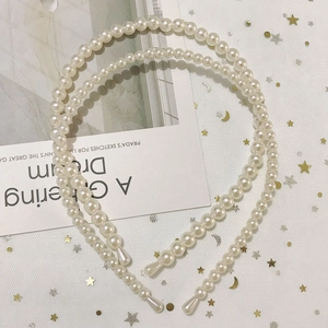 Close-up of two elegant white pearl headbands in different sizes on a starry mesh background