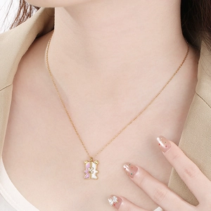 Minimalist gold necklace featuring a pink and white gummy bear pendant on a female model