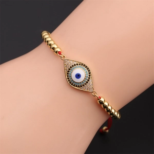 Close-up of sparkling evil eye charm on red braided string bracelet with gold beads