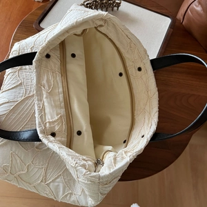 Detail view of cream canvas tote with 3D floral embroidery and black leather strap