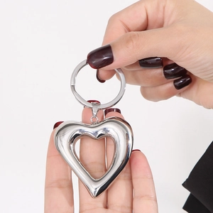 Polished stainless steel hollow heart-shaped keychain held by hand for size scale