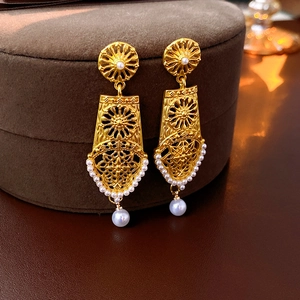 Close-up of gold hollow flower earrings with pearls on a brown suede jewelry box