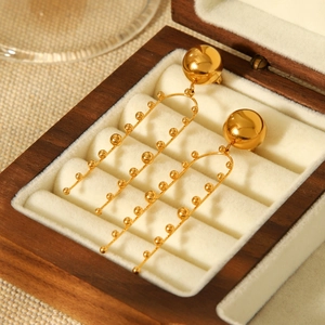 Detail view of U-shaped gold tassel earrings with ball accents in a velvet wooden box