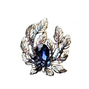 Elegant flower brooch with dark blue teardrop gemstone and golden leaves on white background