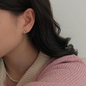 Close-up of heart-shaped 925 sterling silver stud earrings worn with a pearl necklace