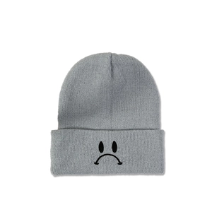 Détail du bonnet en maille grise avec emoji visage triste brodé noir sur le revers