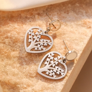 Silver hollow heart earrings with tree of life design on beige stone surface