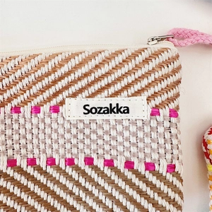Detail of woven straw texture in brown and cream stripes with pink zipper pull