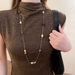 Détail d'un collier de perles en résine vintage sur un pull marron élégant