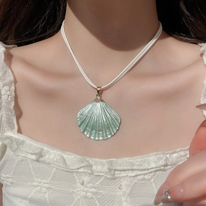 Close-up of cyan shell pendant necklace with gold accents worn on a white lace top