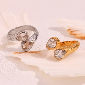 Close-up of gold and silver teardrop open rings with clear gems and water droplets