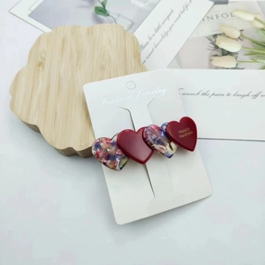 Detail of floral and red acetate heart hair clips with golden label on wooden tray