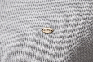 Close-up of a bronze metal brand logo plate on gray knitted fabric texture detail