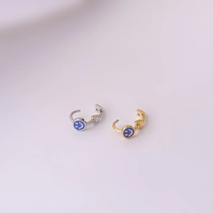 Mini silver and gold smiley face hoop earrings with blue charms on pink background
