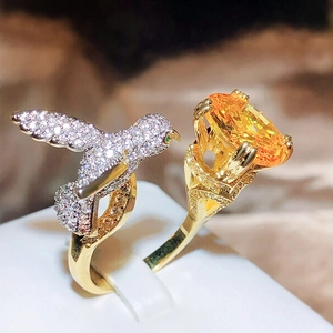 Macro detail of gold hummingbird ring with orange oval gemstone and micro-pavé crystals