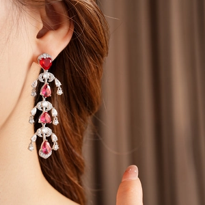 Detail of silver drop earrings with red heart gems and tiered crystal tassels on model