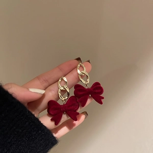 Detail of red velvet bow earrings with golden chain links and vintage aesthetic