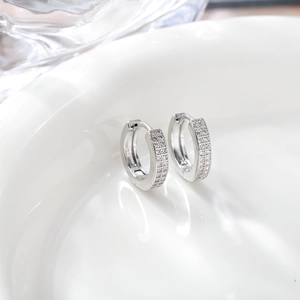 Detailed close-up of silver hoop earrings with pavé-set zircons on a white ceramic tray