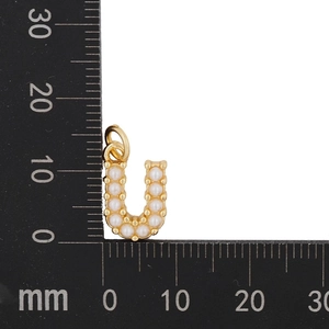 Macro detail of gold U-shaped pendant with pearls measured against a ruler scale