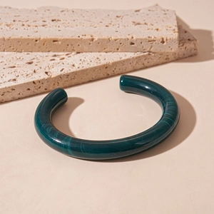 Close-up of dark green resin open cuff bracelet with marble texture on travertine stone