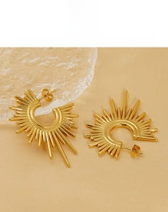 Close-up of golden sunburst C-shape geometric earrings on a soft cream silk fabric background