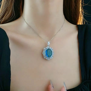 Close-up of a silver necklace featuring an oval blue gemstone pendant with diamond halo