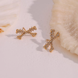Macro detail of gold X-shaped bone earrings with sparkling white pavé crystals on a textured base