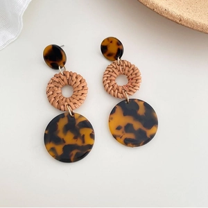 Dettaglio di orecchini boho in resina leopardata e cerchi in rattan naturale intrecciato